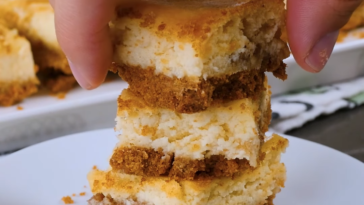 A plate stacked with square slices of cheesecake bar. The cheesecake bars have a graham cracker crust and a light brown cinnamon swirl throughout the top.